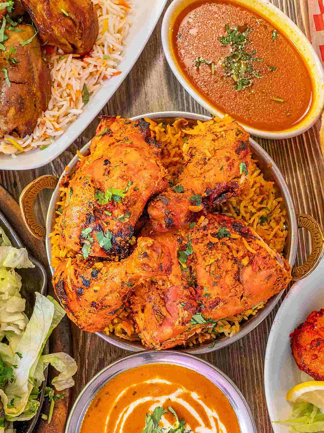 Overhead spread of North Indian dishes at Saffron Indian Bistro Banff — chana masala, butter chicken, pulao rice, naan, samosa and raita